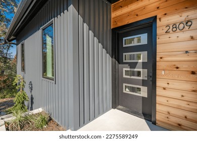 Front door entry exterior of a contemporary home with grey metal siding black entrance and cedar siding