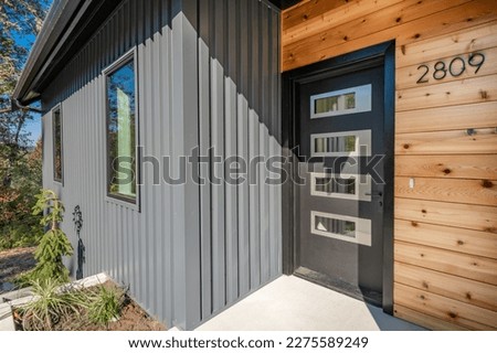 Front door entry exterior of a contemporary home with grey metal siding black entrance and cedar siding