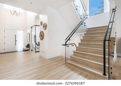 front door foyer entrance to an interior of a home with hardwood flooring beamed ceiling glass wall stair case view to home office and black metal stair railing - Shutterstock ID 2276396187