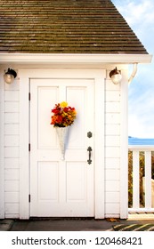 Front Door Of A Seaside Cottage Painted White With Vintage Hardware And Decorated With A Basket Of Flowers. 