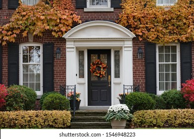 Front Door Of Traditional Brick House With Fall Wreath  Surrounded By Ivy With Fall Colors