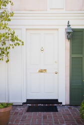 Front Door Of An Upscale Home/Vertical Shot Of A White Front Door With Brass Accents And Green Stutters On A Home With View Of Brick, Mail Slot And Door Mat.