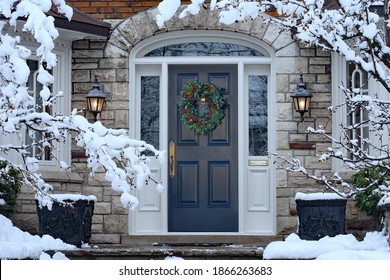 Front door in winter with seasonal wreath, surrounded by snow