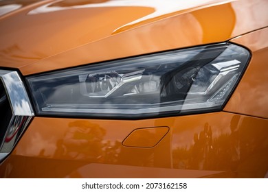 Front edgy car LED headlight. Detail of headlamp with headlight washer. Orange shiny car. Close up. 