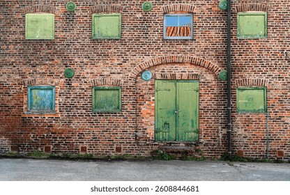 Front elevation brick wall of now disused historical warehouse with green painted boarded windows and one glass window with reflections of sky and roof pantiles in centre. Driffield, Yorkshire, UK.