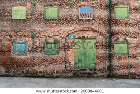 Front elevation brick wall of now disused historical warehouse with green painted boarded windows and one glass window with reflections of sky and roof pantiles in centre. Driffield, Yorkshire, UK.