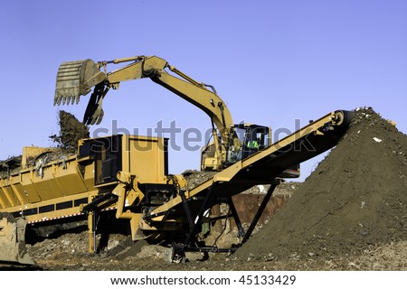 Front end loader dumps landfill into a screener to separate solid waste from good soil which is transported by conveyor belt to preserve landfill space.