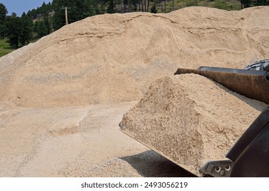 A front end loader making easy work of moving large amounts of gravel in a bucket from a huge crushed stone pile during an engineering project.