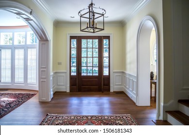 front entrance foyer hallway of a large home house with yellow walls and a wood door with windows and a large custom lighting fixture