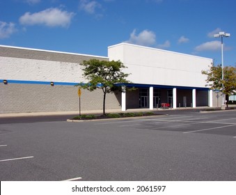 Front entrance of a vacant big box brick and mortar retail store and empty parking lot available for real estate lease or sale