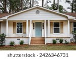 The front exterior entrance of a newly painted white siding brick ranch style house with a large yard that has been recently renovated.