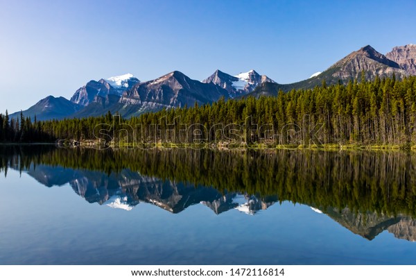 Front facing view of Herbert Lake in\
Banff National Park, Alberta Canada with Rocky mountain range in\
background and glass like reflection in the foreground.\

