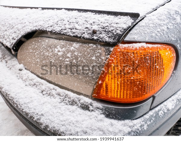 The front headlight of a\
car with an orange turn signal is covered with snow after a\
blizzard, close-up.