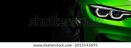 Front headlights of green modern sport car on black background, free space on left side for text.