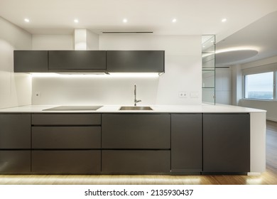 Front Of A Kitchen With Dark Gray Furniture, Oak Parquet Flooring, White Stone Countertop And Glass Cabinet