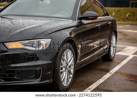 Front left headlight on a modern black car. Black metallic bumper car with light and wheel. Lamp signals for turning a car on street. Exterior automobile closeup. Side view of modern new car.