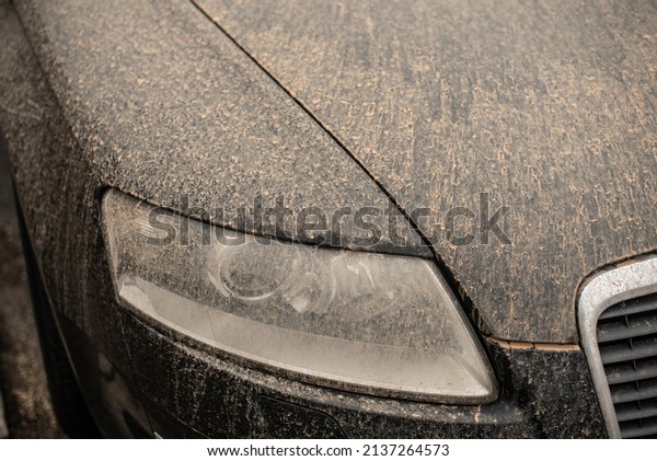 the front light and varnish of\
a black car in Germany after rain polluted with sahara\
sand