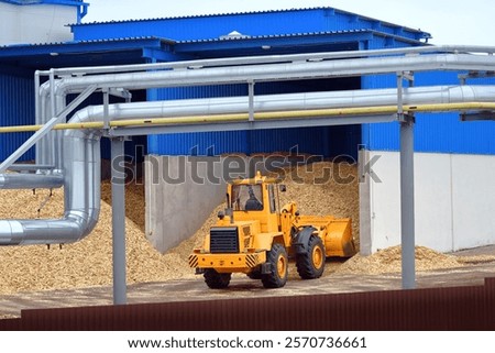 Front loader operating in woodchip storage yard at manufacturing facility. Bulldozer handling woodchips, transporting wood chips at an warehouse, storage operations for pellets manufacturing. Biofuel