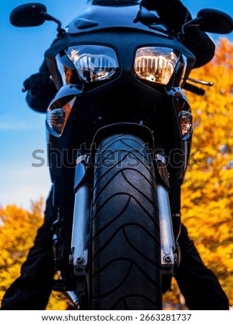 Front low angle view of a powerful black motorcycle parked against a vibrant, blurred background of yellow autumn leaves. A concept of freedom, road trips, adventure, and the beauty of the fall season