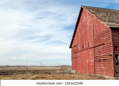 Front of an Old Red Barn by a Harvested Field against a Cloudy Blue Sky