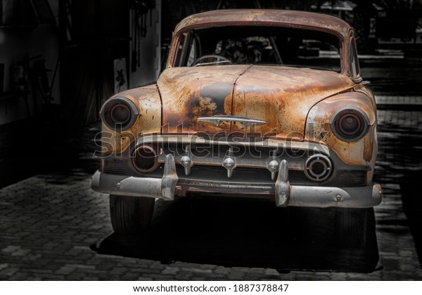 front of a parking\
 antique car with chrome bumper and grill, rusty fenders and hood\
and broken head lamps