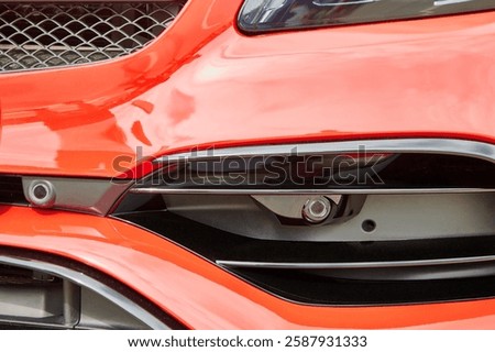 Front parking sensor on a red modern car. Car front bumper with parking sensors.