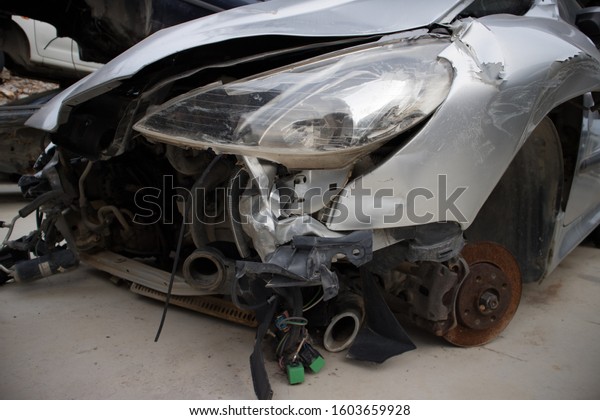 The front part of a crashed car, with silver\
colour. In a vehicle\
graveyard.