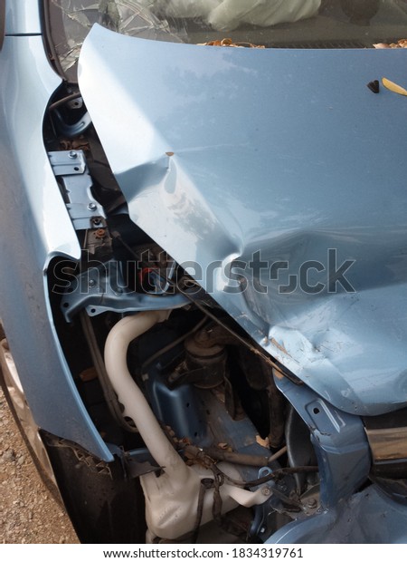 The front part of a crashed car with turquoise\
colour. At a vehicle\
cemetery.