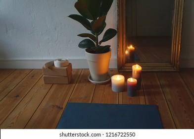 Front Part Of Yoga Mat In Apartment On Wooden Floor, With Candles, Miror, Yoga Blocks, Plant In The Background. No People, Cosy Atmosphere