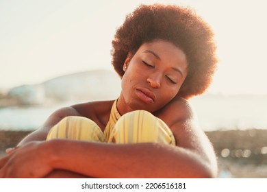 Front Portrait Of Pretty Young Black Girl Relaxing With Closed Eyes In Outdoor With Sunlight In Background. Concept Of Meditation Serene People. Loving Yourself Lifestyle People. Afro Hair Style Model