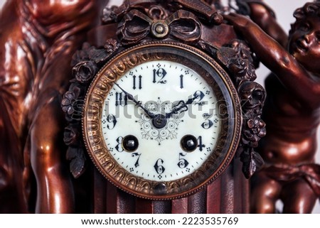 A front portrait of the retro clock face of an old vintage clock made of wood and metal with beautiful clock hands and numbers for indicating the time. It is ten before two.