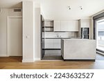 Front of a recently installed modern style kitchen with handleless cabinets, marble island and stoneware floors combined with laminated flooring with access to a glazed terrace