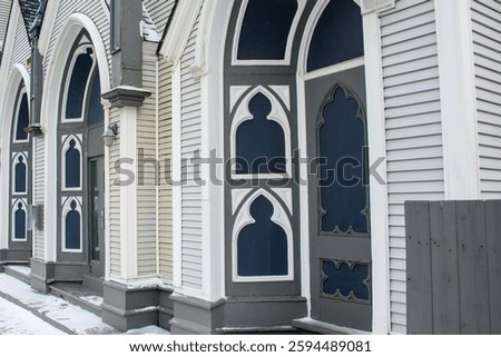 The front of a religious building with multiple arched entranceways. The exterior wall is grey wooden clapboard siding. The wide wooden trim is white. There are black temple decals on the archways.