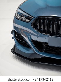 Front right corner of blue sporty car. Close-up view of performance model of modern german car - headlight, grille, bumper and aftermarket body accesories