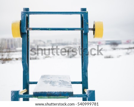 Front shot of a gym workout bench in the foreground and a city in the blurred background