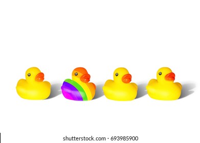 A Front Shot Of A Row Of Three Yellow Rubber Ducks And One Duck Painted In Colors Of A Rainbow Flag (LGBT Pride Flag) On The White Background With Shadows.