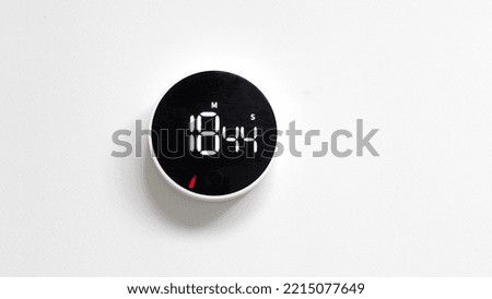 Front shot of white and black minimalistic timer chronometer with reverse time response, on white wall with copy space for advertising text. The countdown has started. Fast flowing time concept.