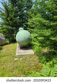 The Front Side Of A Large, Commercial Grade Propane Tank. The Tank Is Circular And Painted A Pale, Pastel Green. There Is A Bright Yellow Pipe Attached To The Top Of It.