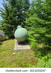 The Front Side Of A Large, Commercial Grade Propane Tank. The Tank Is Circular And Painted A Pale, Pastel Green. There Is A Bright Yellow Pipe Attached To The Top Of It.