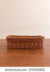 Front side view of an empty rectangular woven basket placed on a wooden table against a neutral background. 
