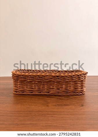 Front side view of an empty rectangular woven basket placed on a wooden table against a neutral background. 
