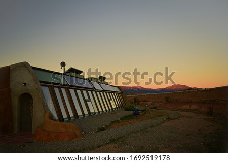 Front side view of self sustaining eco-friendly Earth ship home at sunset with mountains in background of landscape in Toas, New Mexico.