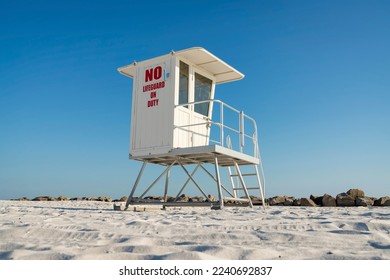 Front side view of a white lifeguard tower against the rocks and blue sky at Destin, Florida. Lifeguard tower with glass panel at the front on a white sand beach.