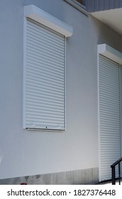 Front Of The Store With Closed White Roller Shutters. The Entrance To The Store And The Windows Are Closed With Protective Aluminum Shutters. Rubbish And Dirt On The Floor. Economic Crisis, Bankruptcy