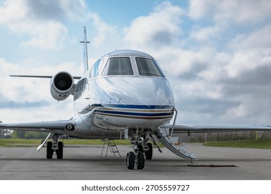 Front three-quarter view of q white small corporate business jet with the boarding stairs extended. Cloudy blu sky in the background.