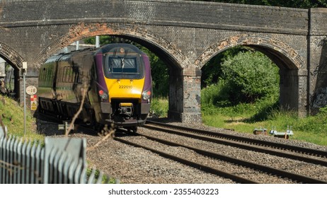 The front of a train going under an old fashioned style brick bridge.