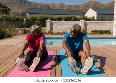 Front view of an active African American senior couple performing stretching exercise next to the swimming pool in the backyard of home - Powered by Shutterstock