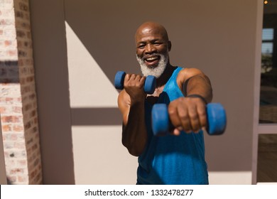 Front view of active senior African American man training arms with dumbbells in the backyard of home - Powered by Shutterstock