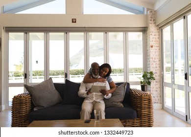 Front view of active senior couple using digital tablet in living room at home