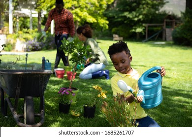 Front view of an African American boy in the garden watering plants, with his parents gardening in the background. . Social distancing and self isolation in quarantine lockdown for Coronavirus Covid19 - Powered by Shutterstock